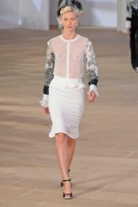 Юбка-карандаш белого цвета с оборкой на нижнем крае от Preen 2012 с полупрозрачной блузкой белого цвета и серо-чёрным растительным принтом Preen и чёрными туфлями на каблуке Preen