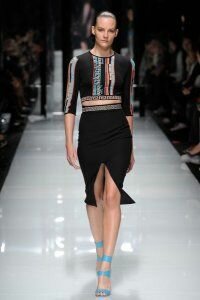 Юбка-карандаш чёрного цвета с разрезом спереди от Versace 2011 с обтягивающим укороченным топом чёрного цвета с яркими вставками Versace и босоножками голубого цвета на высоком каблуке Versace